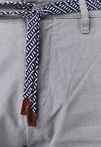 Grå byxor med ett vävt bälte i marinblått och vitt mönster med bruna läderändar. Synlig struktur i tyget nära midjan.