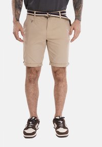 Pantaloni corti beige con risvolti, dotati di chiusura frontale con bottone e zip. Abbinati a una cintura a righe e scarpe da ginnastica marroni.