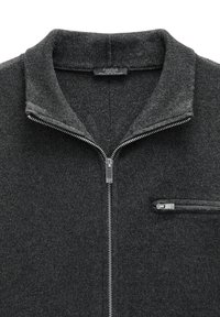 Czarnoszary sweter dzianinowy z pełnym suwakiem z przodu, stójką oraz zamykaną kieszenią na piersi po prawej stronie.