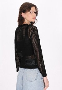 Schwarzer Strickpullover mit Mesh-Design, langen Ärmeln und rundem Ausschnitt. Kombiniert mit einem hellen Jeansrock, der einen lässigen Stil zeigt.