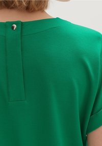 Grønt kortærmet top lavet af glat stof, med knaplukning på ryggen og et rent, minimalistisk design med diskret syning.