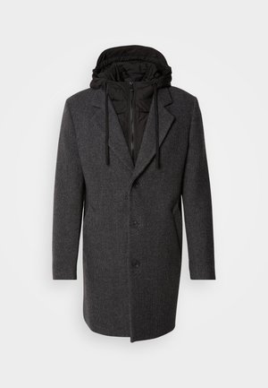 Manteau long gris avec un col structuré, doté d'une capuche en doudoune noire amovible, une fermeture à double bouton, et un motif de tissu texturé.