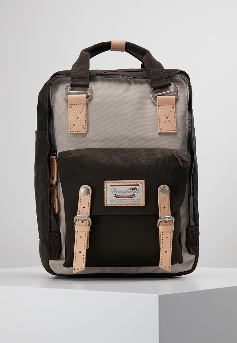 Mochila que presenta una combinación de materiales marrón oscuro y gris claro, con correas y herrajes de cuero beige, forma rectangular y bolsillo frontal.