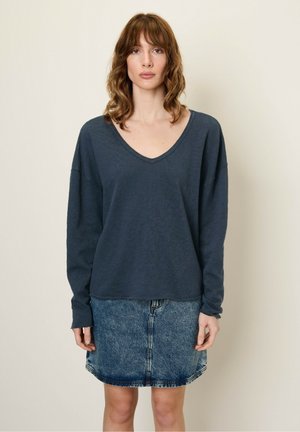 Un haut gris foncé à manches longues en V, fabriqué en tissu doux, associé à une jupe en denim bleu avec un design classique à cinq poches et un ourlet effiloché.