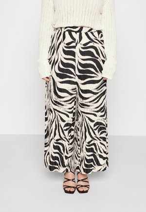 Hvide, plisserede bukser med vid ben og sorte zebra-striber, båret sammen med en cremefarvet strikketrøje og sorte hæl-sandaler med stropper.