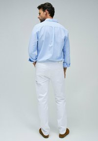 Camicia azzurro chiaro a maniche lunghe abbinata a pantaloni bianchi. I pantaloni presentano una tasca posteriore con zip, un tessuto liscio e una vestibilità slim.