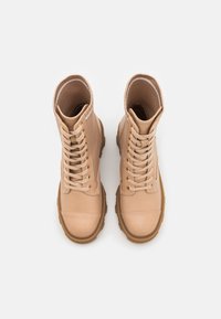Botas de tobillo beige con un upper de cuero suave, suela de goma gruesa y ojales reforzados. Diseño con cordones y cuello acolchado.