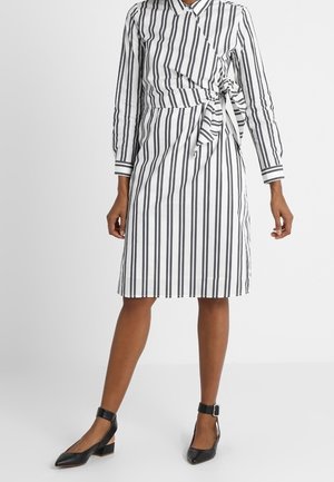 Zwart-wit gestreepte jurk met lange mouwen, een wikkelontwerp en een gestrikte taille. Gecombineerd met zwarte ballerina's met enkelriempje.