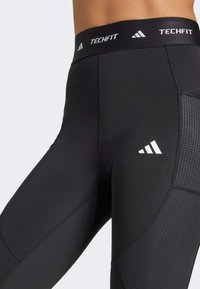 Leggings atléticos negros con un diseño ajustado, una cinturilla ancha etiquetada como "TECHFIT" y paneles texturizados con un patrón en rejilla.