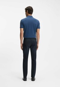 Mäns marinblå polo med kort ärm, kombinerad med mörka denimjeans. Slät textur, åtsittande design och synlig bakfickdetalj.