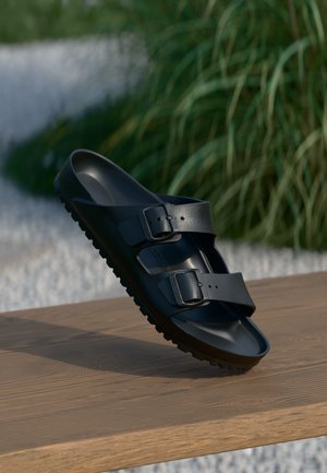 Black two-strap sandal with adjustable buckles, made from flexible material, featuring a textured sole and smooth upper surface.