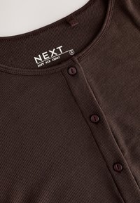 Cardigan côtelé marron avec un col rond, doté de boutons et d'une étiquette indiquant "NEXT Soft Rib Cardi".