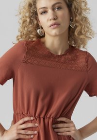 Robe couleur rouille à manches courtes, corsage texturé et motif en dentelle au niveau de l'encolure. Dotée d'une taille élastique pour une silhouette ajustée.