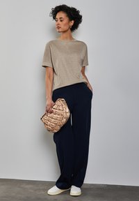 Top beige a maniche corte abbinato a pantaloni larghi blu navy. Tiene una borsa in crema intrecciata. Sneakers bianche su un pavimento grigio. Design semplice e pulito.