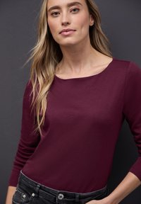 Burgundowy top z długim r�ękawem o okrągłym dekolcie, wykonany z miękkiego materiału, w zestawieniu z czarnymi spodniami z detalami w postaci srebrnych guzików.