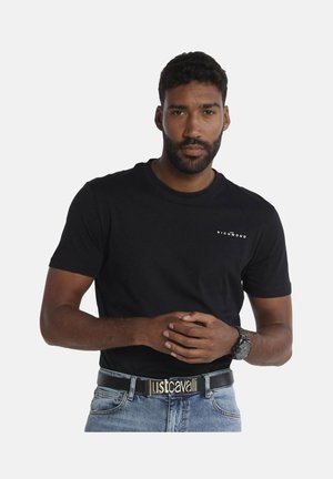 T-shirt nera in cotone con scollatura rotonda e piccolo logo bianco "RICHMOND". Indossata con jeans blu e una cintura nera con la scritta "justcavalli" in oro.