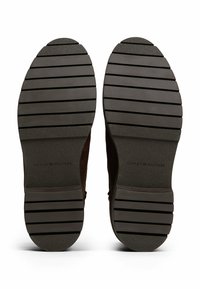 Suole di scarpe marroni scure con linee di battistrada in gomma orizzontali e "Tommy Hilfiger" impresso su ciascuna suola.