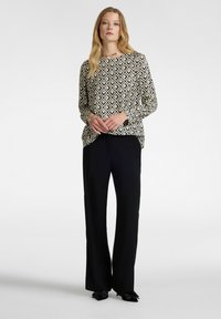 Långärmad topp med ett svart och beige geometriskt mönster, tillsammans med svarta vida byxor och svarta skor med rosettdetalj.