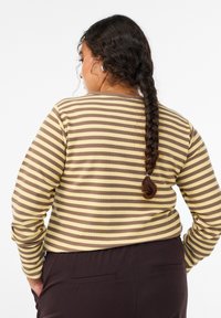 Długi rękaw koszuli ribbed w poziome paski w kolorze żółtym i brązowym, okrągły dekolt i luźny krój. Widok z tyłu z warkoczem.
