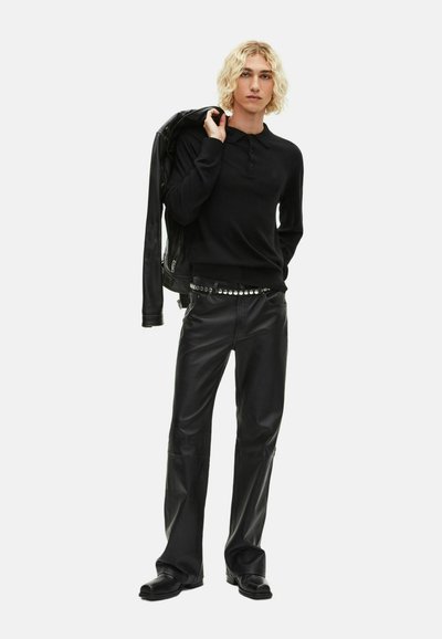Polo nero a maniche lunghe con chiusura a tre bottoni, abbinato a pantaloni in pelle nera e una giacca in pelle abbinata appoggiata sulla spalla.