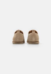 Chaussures en daim beige avec une texture lisse, à bout rond et à talon fin. L'arrière est doté d'une boucle pour un enfilage facile. Design simple et épuré.