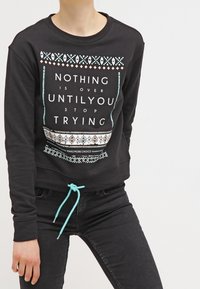 Sudadera negra con cuello redondo y dobladillo corto, que presenta un estampado tipográfico en blanco y turquesa, además de acentos estampados en la parte inferior.