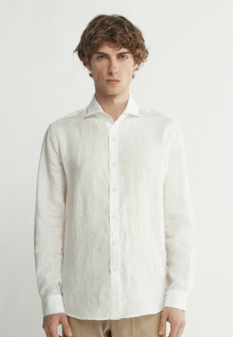 Chemise en lin blanche à manches longues, avec un devant à boutons et un col classique. Le tissu texturé donne une apparence légère.