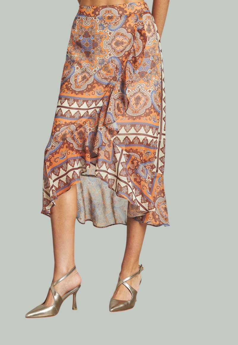Jupe fluide et à motifs dans des tons d'orange, de bleu et de crème, avec un ourlet asymétrique. Portée avec des chaussures à talons hauts dorées en métal avec des lanières croisées.