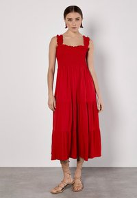 Rotes, ärmelloses Maxikleid mit gerafftem Oberteil und Rüsche-Trägern. Ausgestellter, gestufter Rock fällt unter das Knie. Kombiniert mit beigen Riemchensandalen.