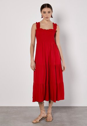 Rotes, ärmelloses Maxikleid mit gerafftem Oberteil und Rüsche-Trägern. Ausgestellter, gestufter Rock fällt unter das Knie. Kombiniert mit beigen Riemchensandalen.