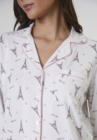 Pigiama bianco con profili rosa, caratterizzato da un motivo di torri Eiffel e cuori. Tessuto leggero e morbido, con taschino sul petto e chiusura a bottoni.