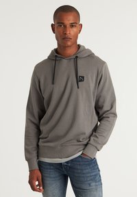 Grijze hoodie met een trekkoord, kangoeroezak en een klein zwart logo-opdruk op de borst. Zacht, soepel materiaal, gecombineerd met een blauwe spijkerbroek.