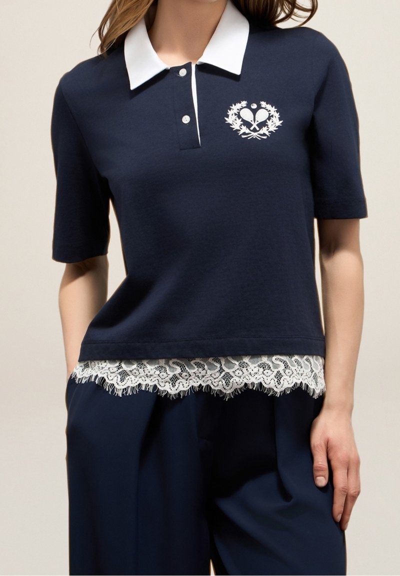 Polo shirt à manches courtes marine avec un col blanc et un bord en dentelle à l'ourlet. Présente un design de cœur et de laurier en blanc.