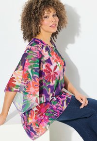 Tunika blusa fluida e trasparente con vivaci motivi floreali nei toni di rosa, verde, viola e arancione. Presenta maniche ampie e un collo rotondo.
