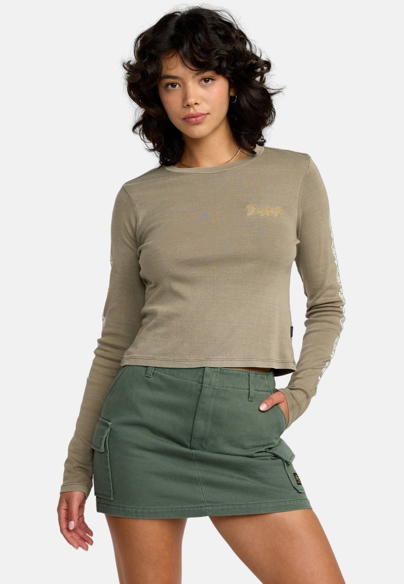 Langemouwige, olijfgroene cropped top met gouden logo, gecombineerd met een groene minirok in cargostijl met zakken en stiksels.