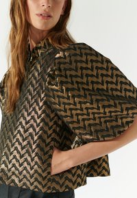 Blusa a maniche corte in oro e nero, caratterizzata da un motivo geometrico a scacchi. Realizzata in un materiale lucido con una silhouette strutturata.
