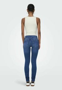 Slim jeans i mørkeblå denim med høj talje. Har to baglommer og en stram pasform ned til anklerne, parret med hvide sneakers.