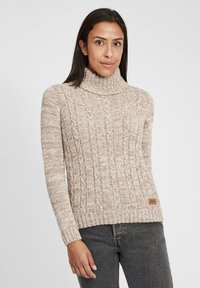 Beige kabelgebreide turtleneck trui met ribbel detailing, voorzien van een klein bruin leren logo patch aan de onderkant.