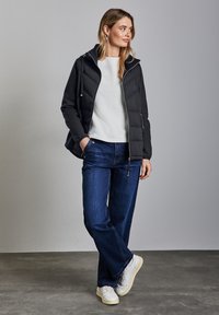 Svart pufferjacka med dragkedja fram och huva, tillsammans med en vit tröja och blå vida jeans. Vita sneakers fulländar outfiten.