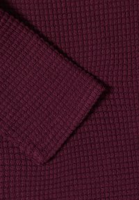 Tissu en maille gaufrée de couleur bordeaux profond avec une manche repliée montrant la texture et un motif sans couture.