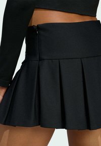 Čierna plisovaná sukňa s pevnou páskou a zipsovým uzáverom. Vyrobená z hladkej látky s jemnou textúrou.