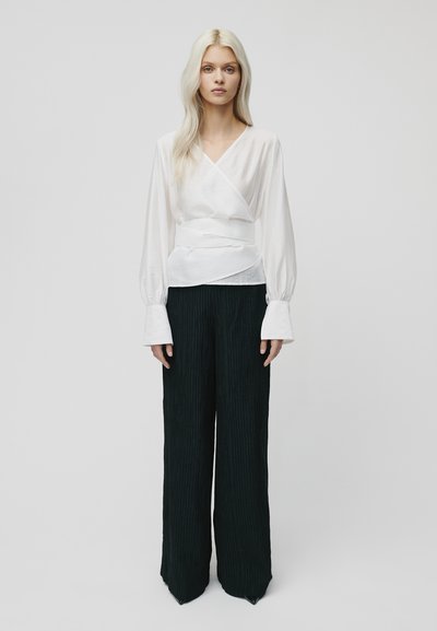 Witte blouse met lange, volumineuze mouwen, gecombineerd met hoge taille, wijde zwarte broek met verticale ribbelstructuur.