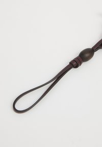 Bracelet en cuir brun foncé avec un accent en perle en bois circulaire et une poignée en boucle, présentant une texture lisse et un design simple.