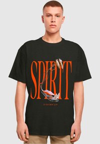 Juodas medvilninis marškinėliai su dideliu oranžiniu užrašu "SPIRIT" ir kąsnomis su aštriais dantimis grafika. Trumpomis rankovėmis, laisvas siluetas.
