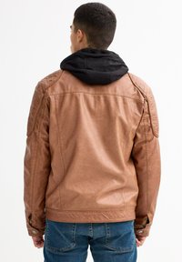 Chaqueta de cuero sintético marrón con diseño de hombros acolchados, capucha negra y puños con botones a presión, combinada con jeans de mezclilla azules.