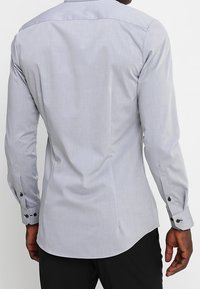 Vaaleanharmaa pitkähihaisen paidan sileä pinta, jossa on kaareva helma ja mustat nappikoristeet hihansuissa.