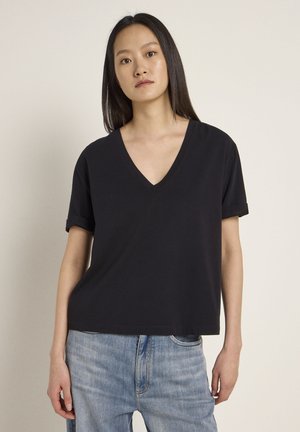 Black, short-sleeved V-neck t-shirt made of soft cotton. The design is relaxed-fit with rolled sleeve cuffs, paired with light blue denim jeans.