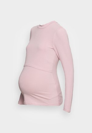 Haut de maternité rose pâle à manches longues avec tissu superposé sur le ventre sur un mannequin sans tête sur fond gris uni.