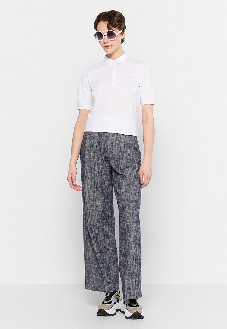 Weißes Polohemd mit kurzen Ärmeln und Knopfleiste, kombiniert mit lockeren, strukturierten navyblauen Hosen; übergroße runde Sonnenbrille und Sneaker.