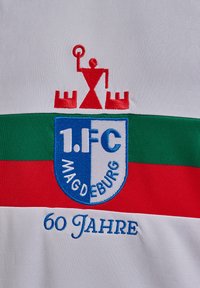 Tessuto bianco con uno scudo blu centrale con la scritta "1.FC MAGDEBURG", strisce orizzontali rosse e verdi e un emblema rosso sopra. "60 Jahre" in blu.